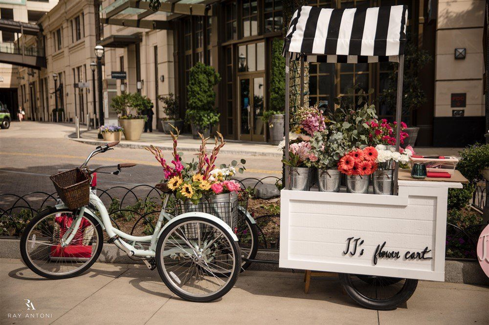 A bicycle is parked next to a cart filled with flowers.