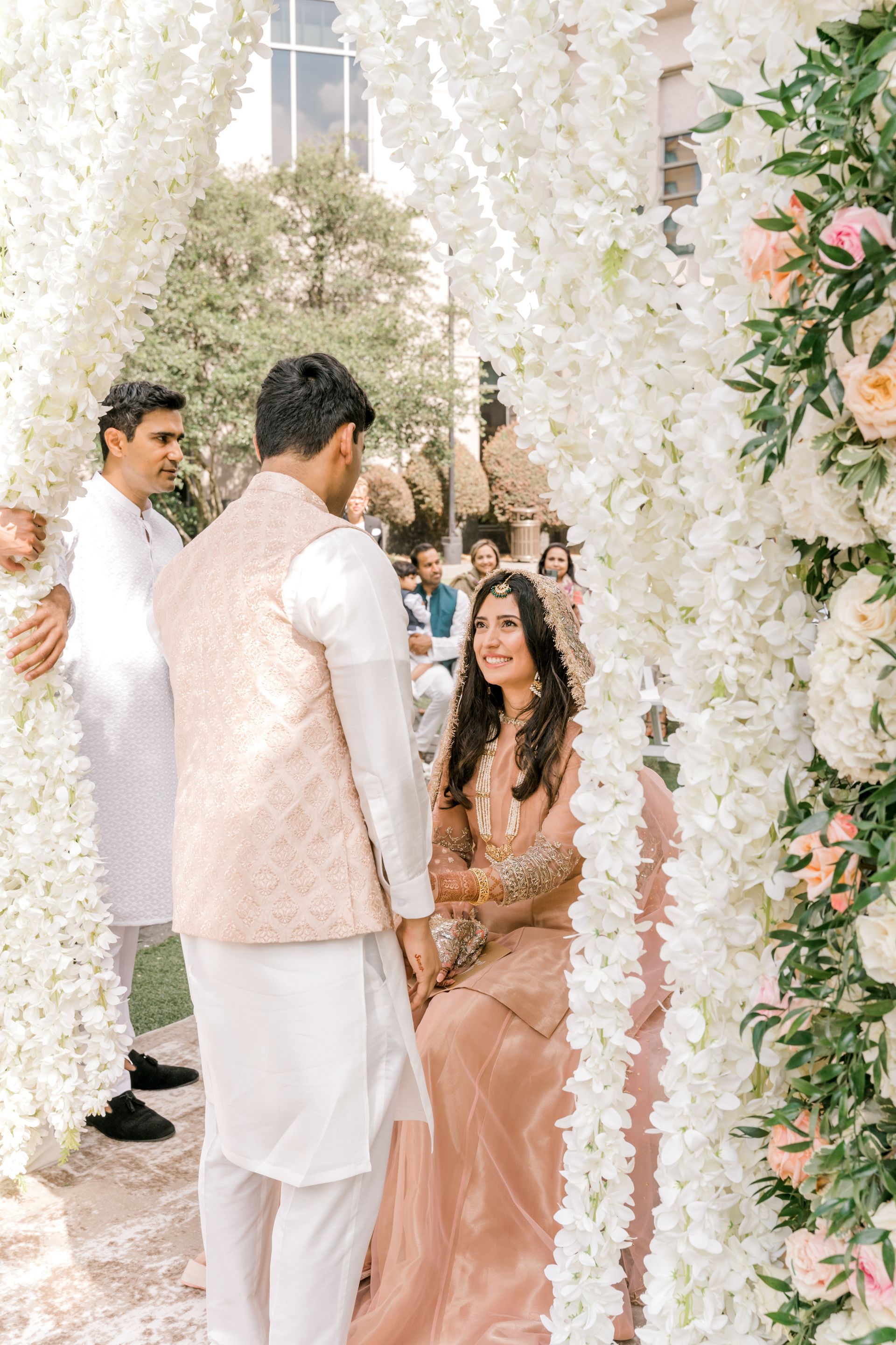 A man and a woman are standing under a white flower arch.