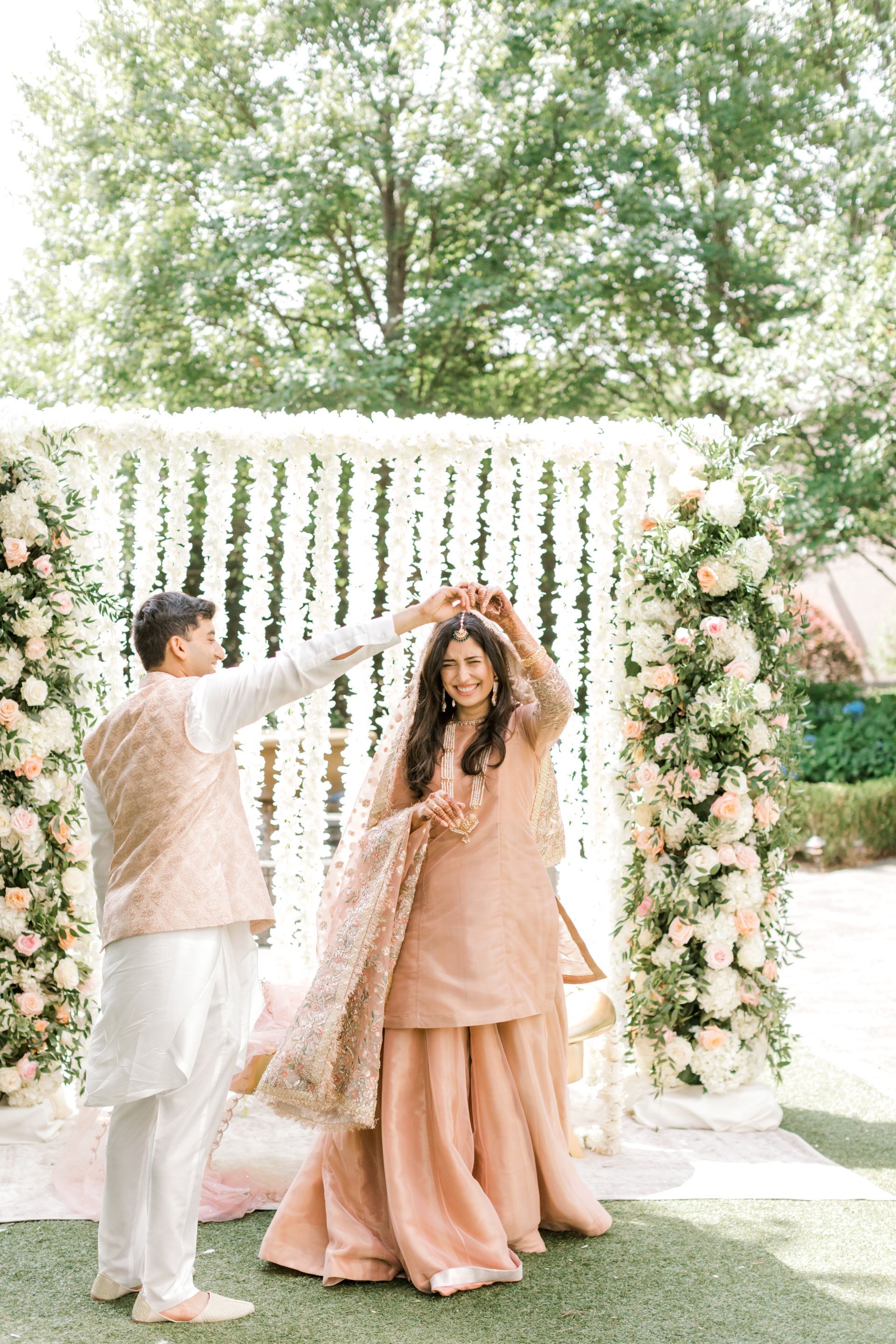 A bride and groom are dancing in front of a floral arch.