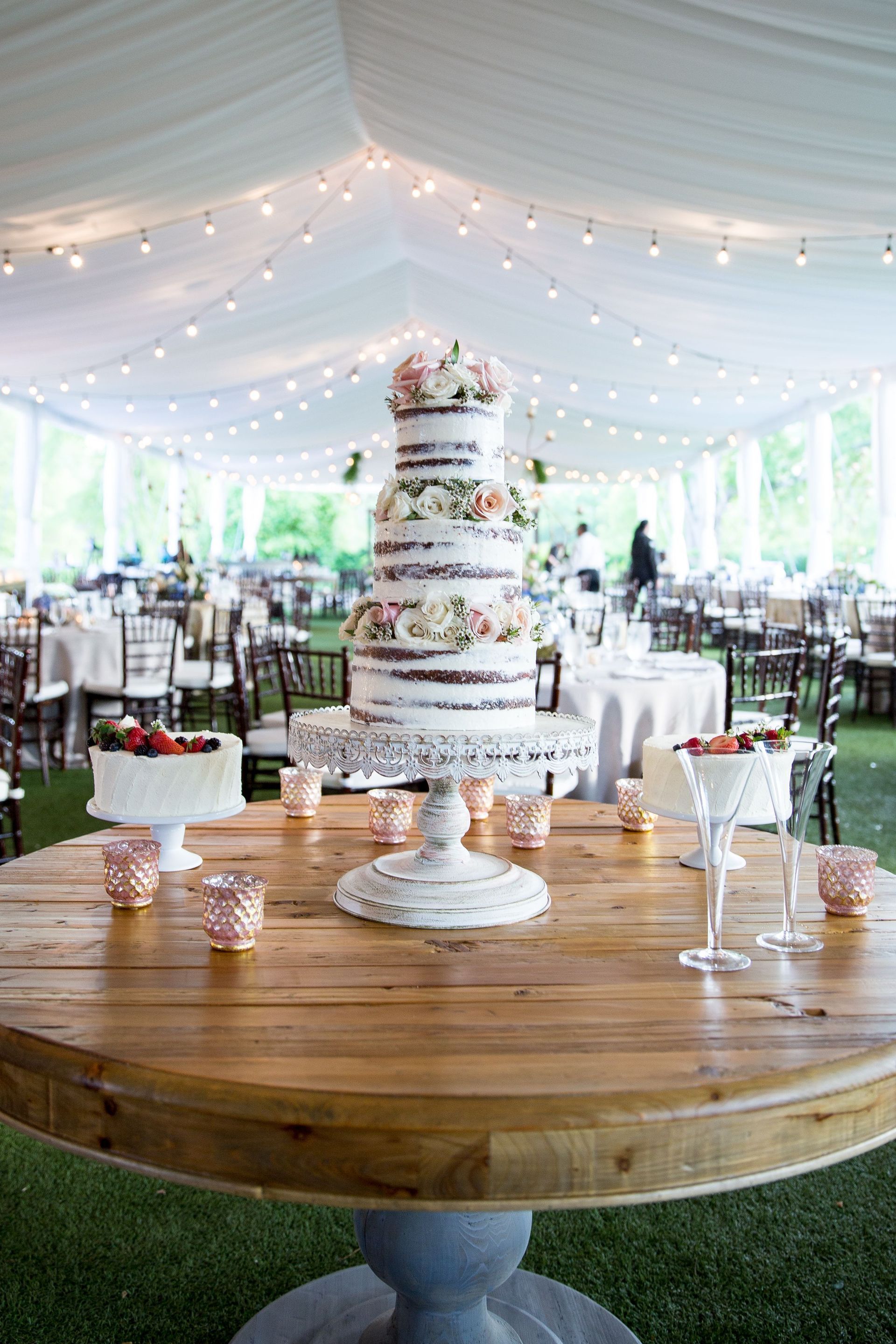 A wedding cake is sitting on top of a wooden table in a tent.