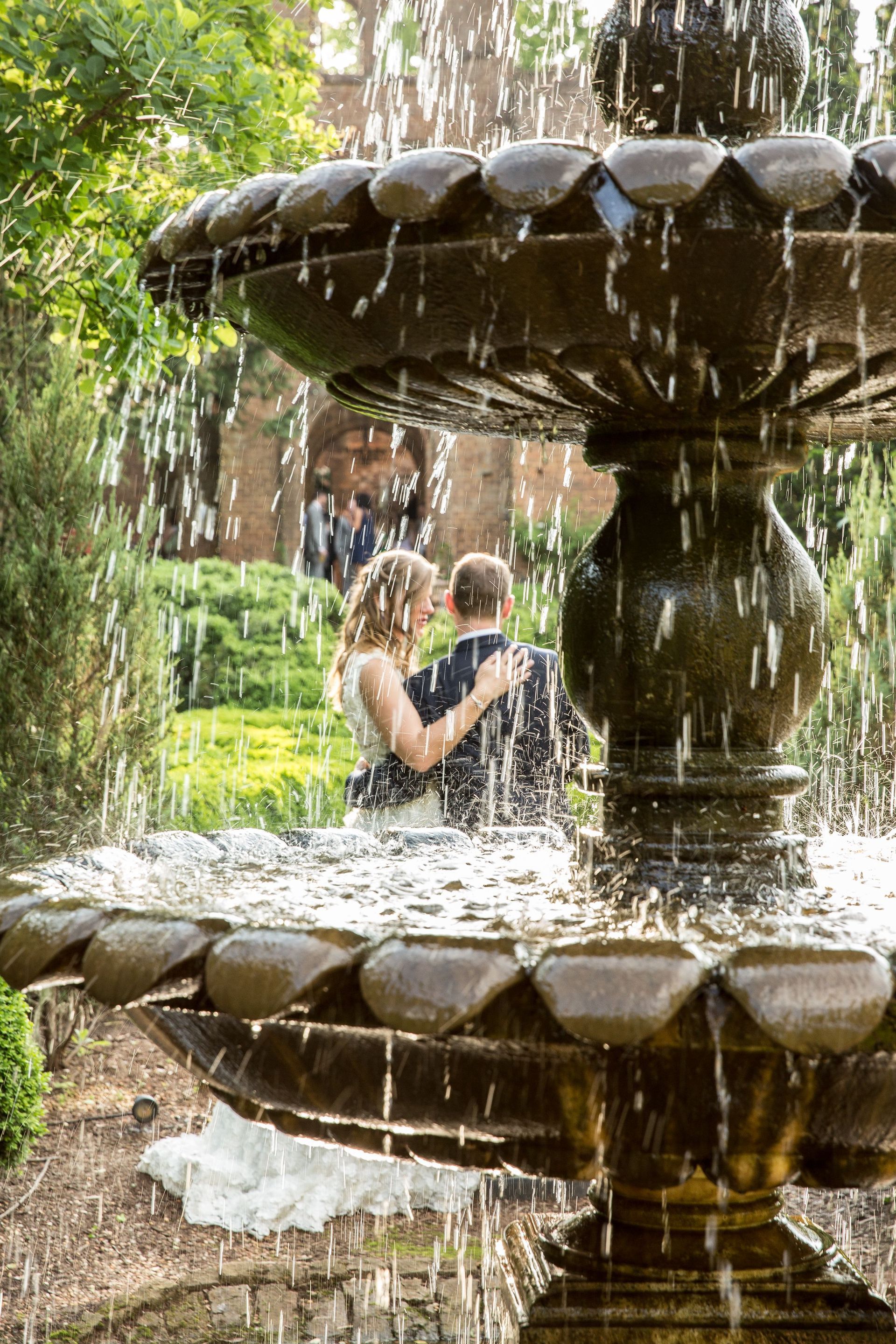 A bride and groom are kissing in front of a fountain.