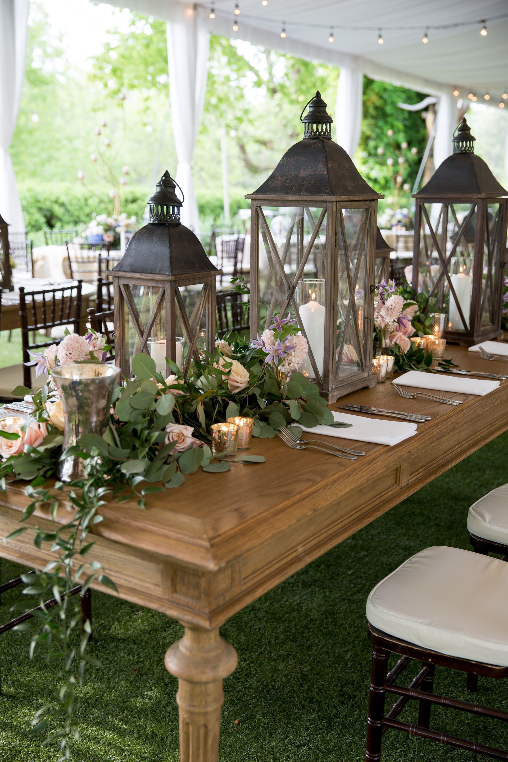 A long wooden table with lanterns and flowers on it under a tent.