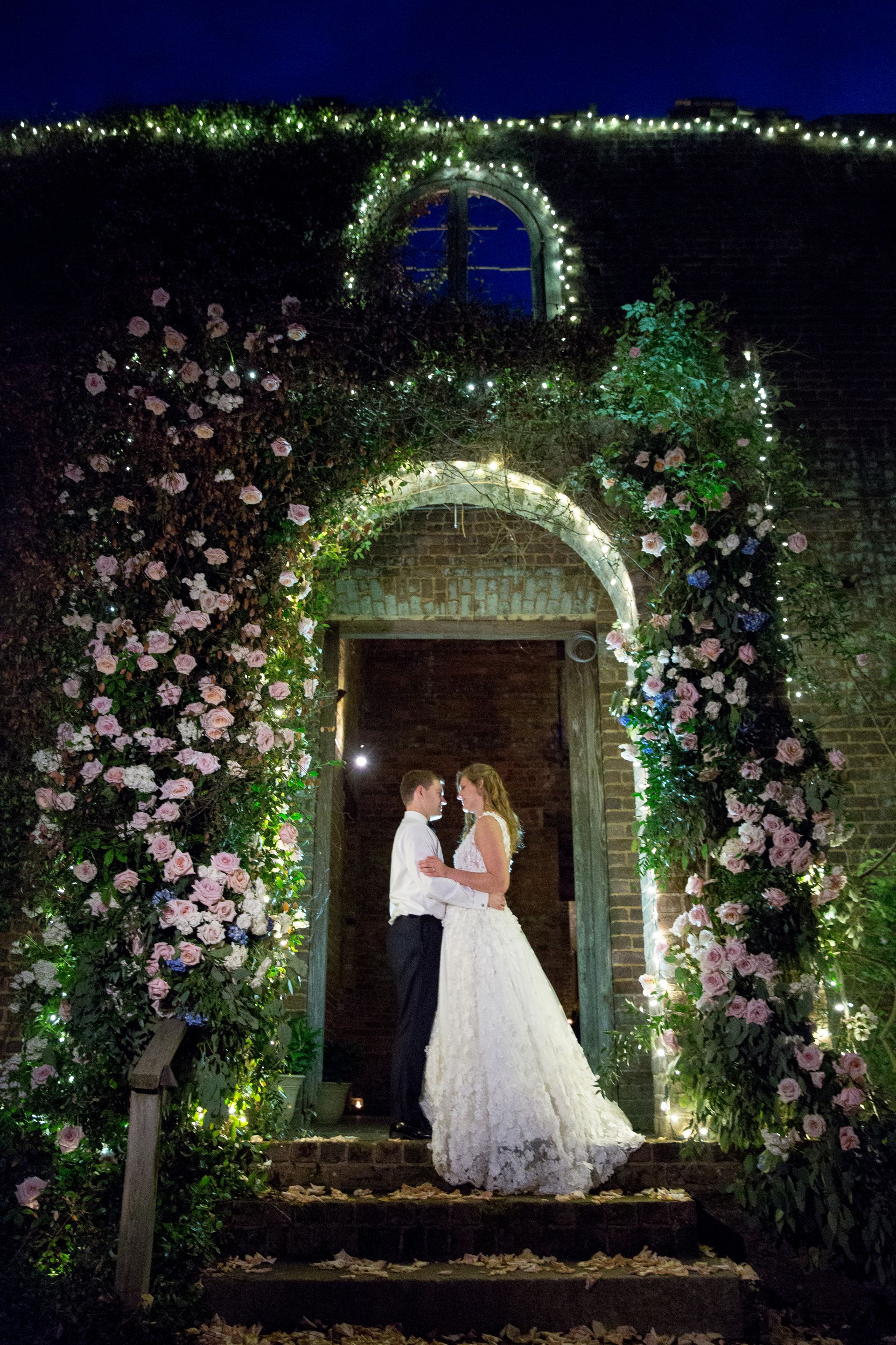 A bride and groom are standing in front of a building at night.