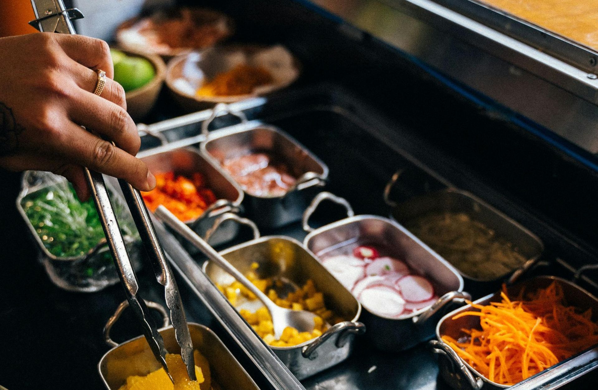 A person is reaching into a tray of vegetables with tongs.