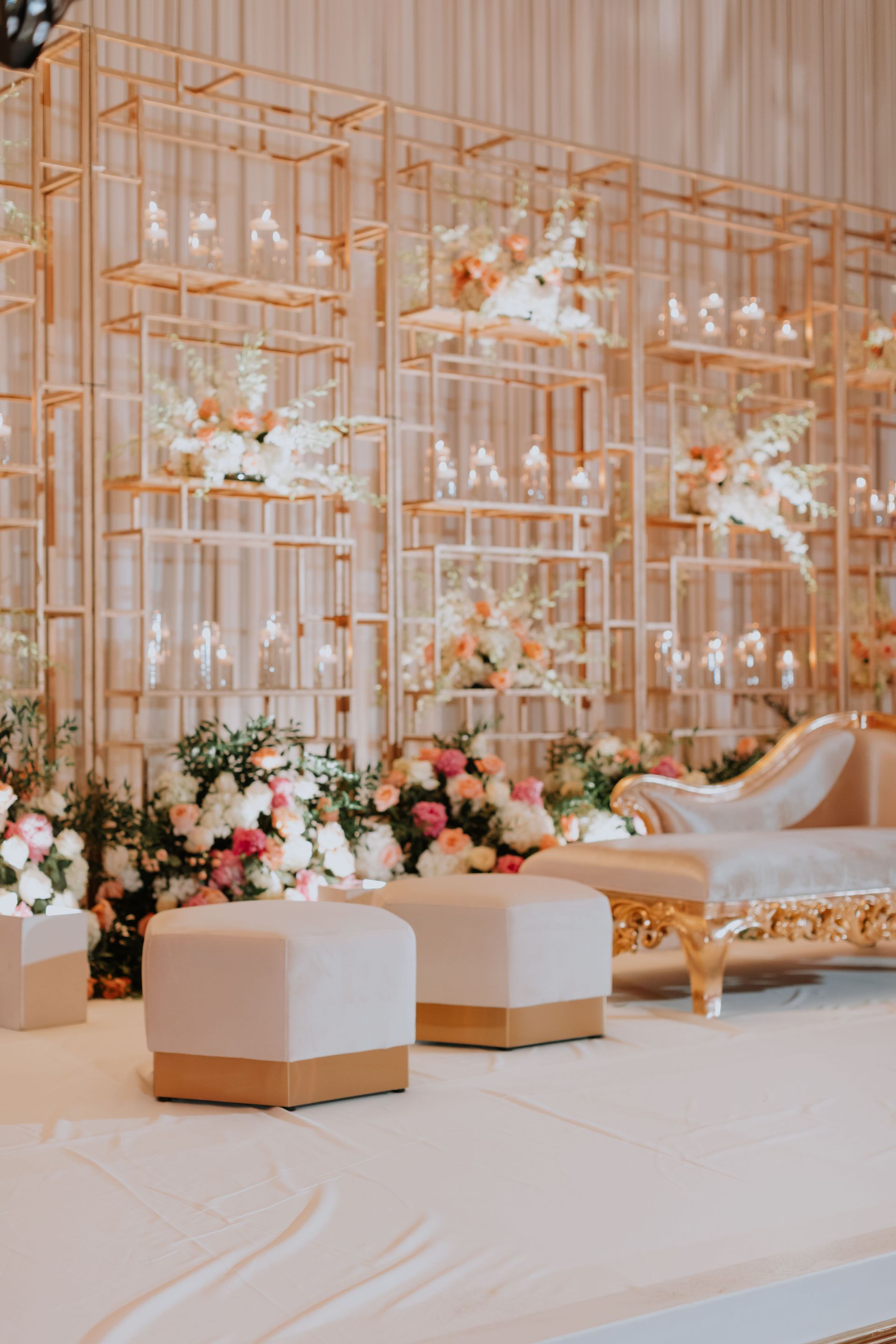 A wedding stage with a couch , ottomans , flowers and candles.