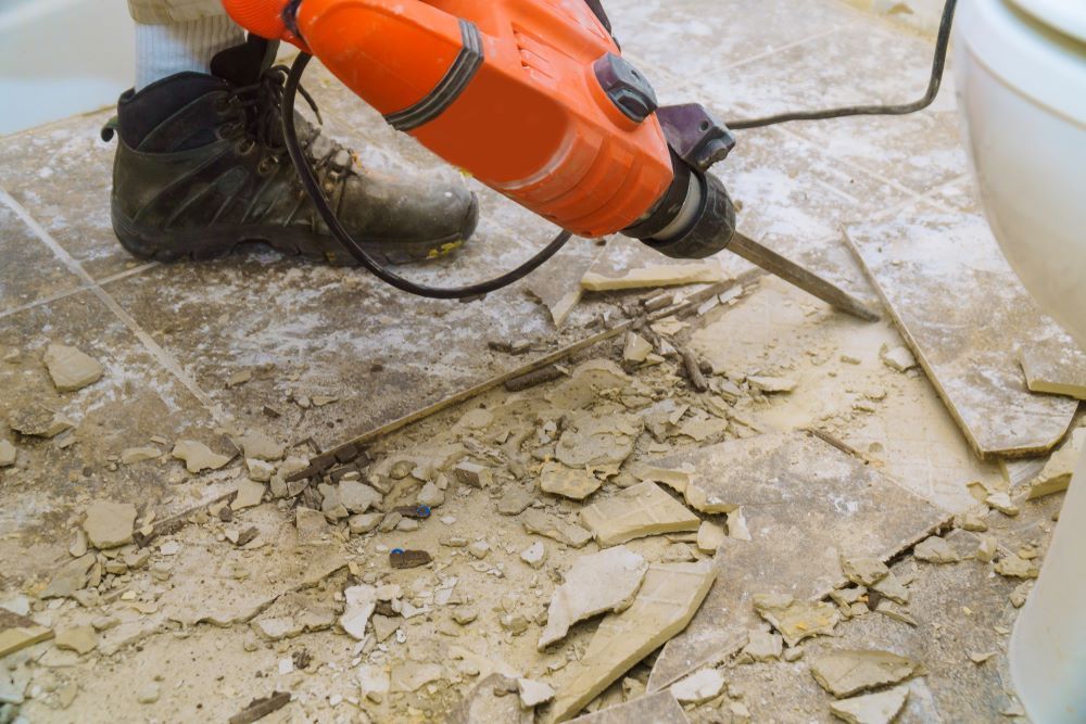 A Person Is Using a Jack Hammer to Remove Tiles from The Floor — Hyper Cut & Drill in Gosford, NSW