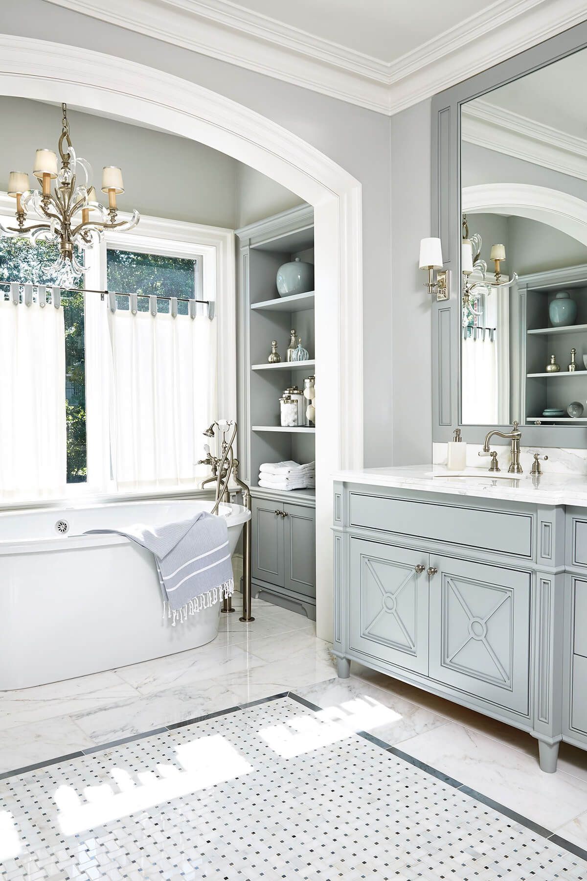 Elegant blue and white bathroom with a soaking tub, vanity, and built-in shelving.