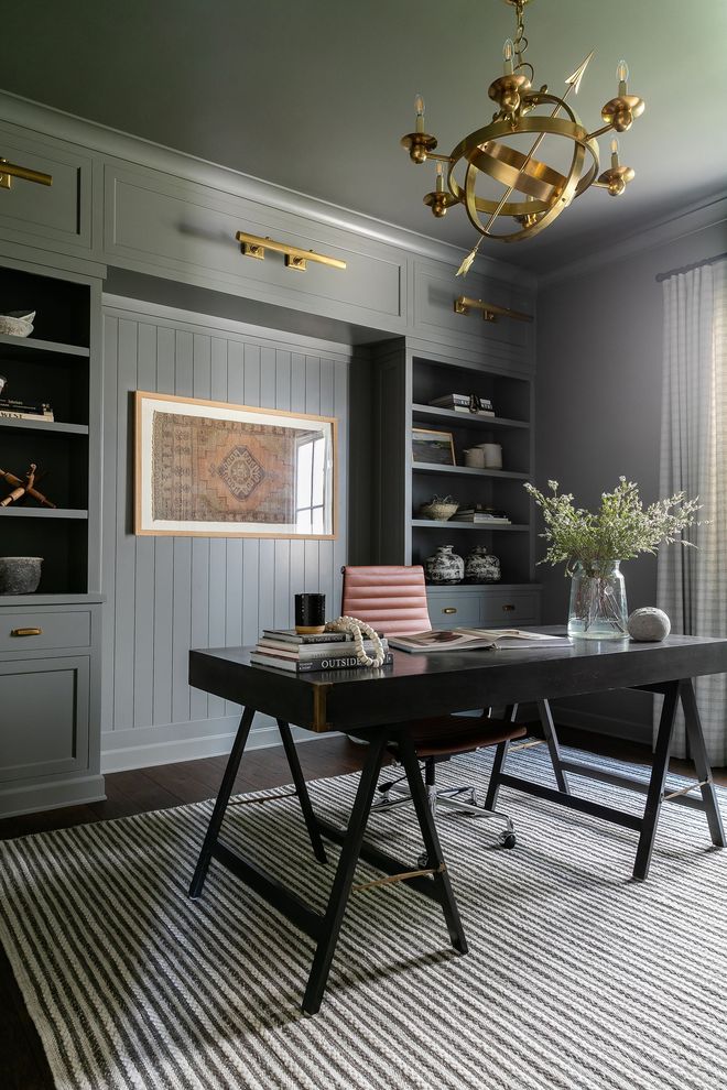 Elegant home office with built-in bookshelves, dark desk, and ornate chandelier. Dark gray walls, light rug.