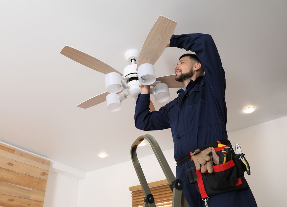 A man is installing a ceiling fan in a living room.