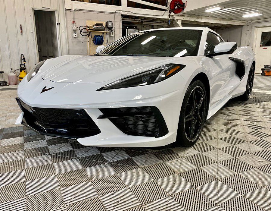 A white corvette is parked in a garage on a checkered floor.