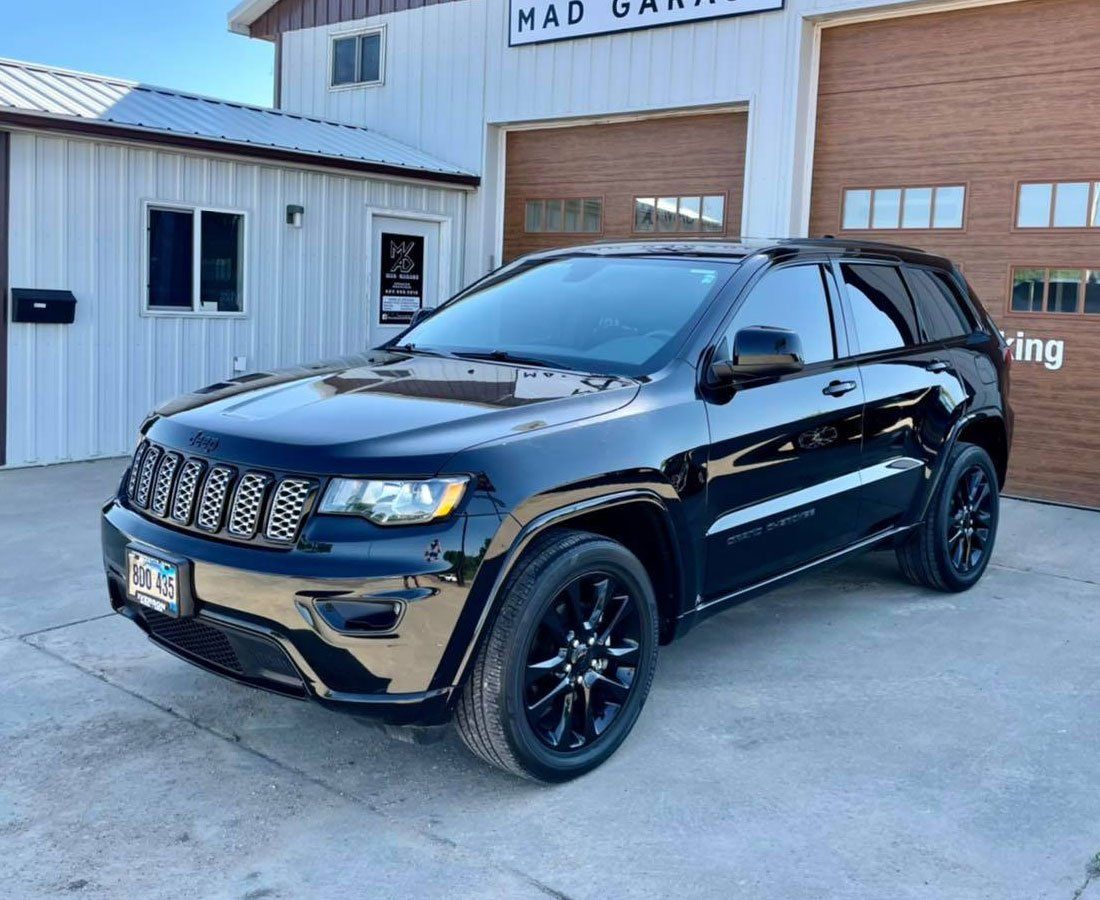 A black jeep grand cherokee is parked in front of a garage door.