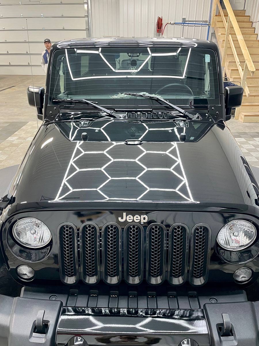 A black jeep with a honeycomb design on the hood is parked in a garage.