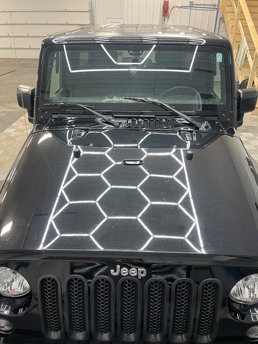 A black jeep with a honeycomb design on the hood is parked in a garage.