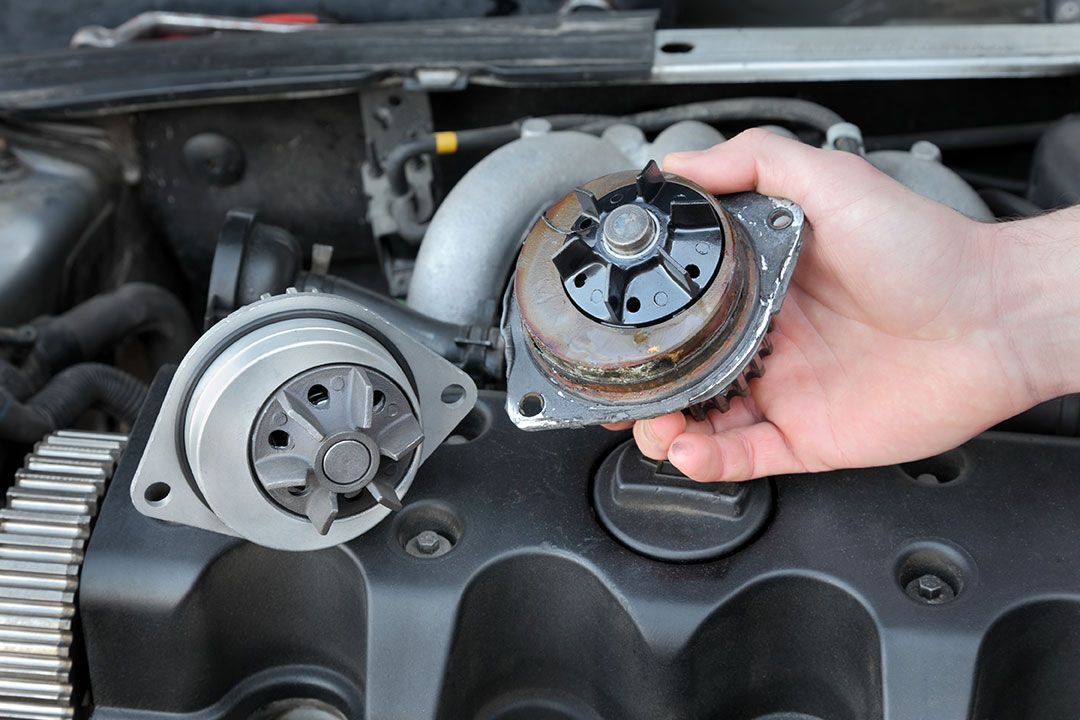 Hand holding a worn metal engine timing gear beside an exposed engine bay