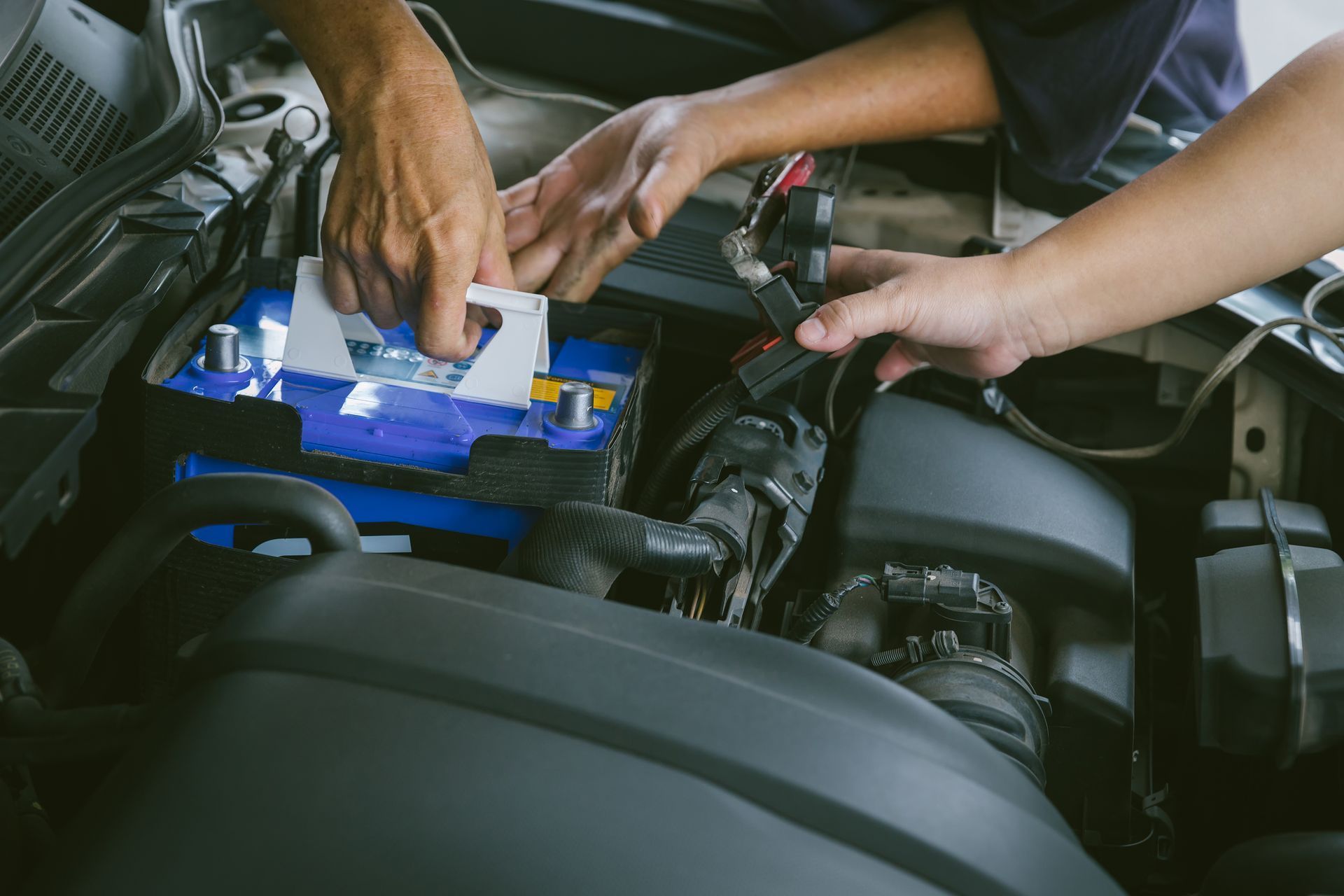 Mechanic replacing a car battery in an engine bay with blue battery lighted by a flashlight