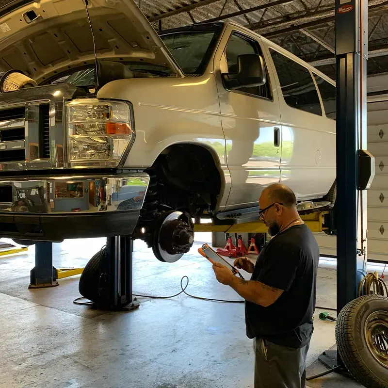 White SUV on a lift in auto shop while mechanic checks a device nearby
