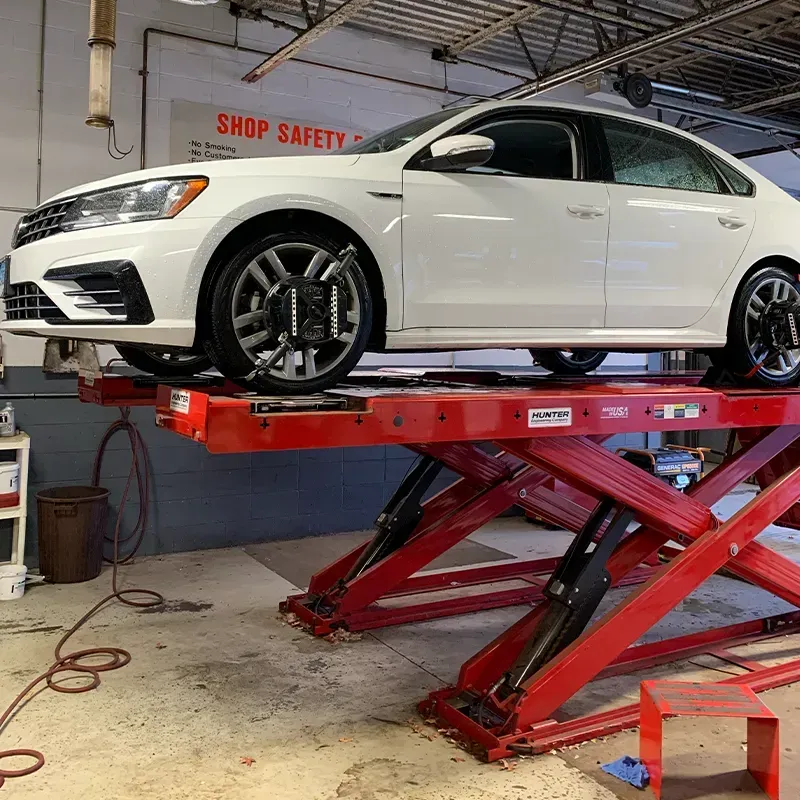 White sedan on a red scissor lift in an auto shop garage.