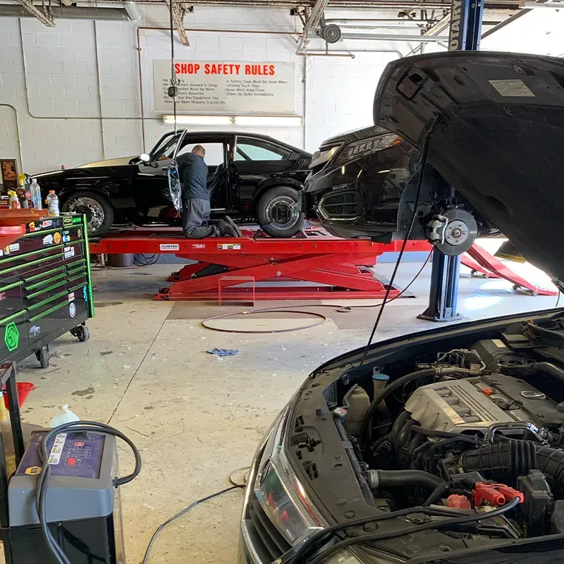 Auto repair shop with a car on a red lift and mechanics working nearby, hood open in foreground