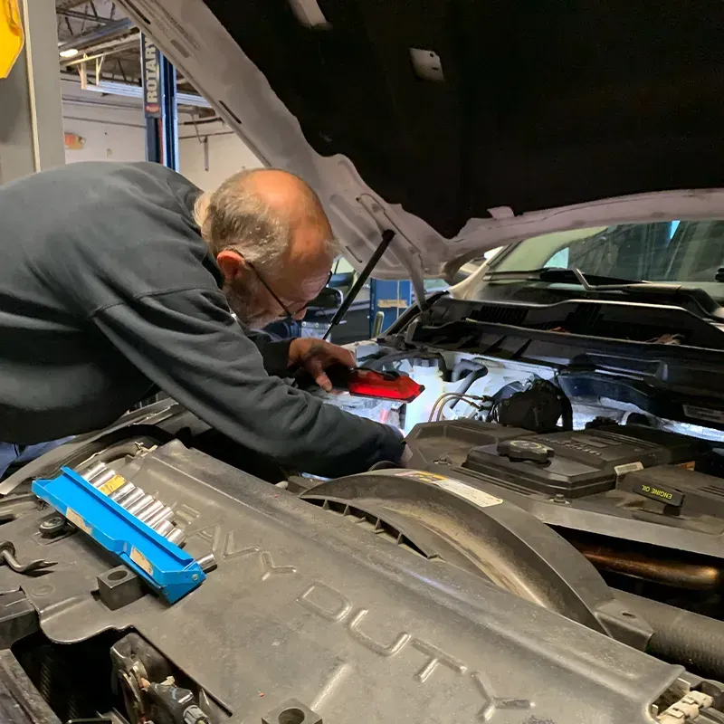 Mechanic working under a car hood in a garage, inspecting engine components with the hood open