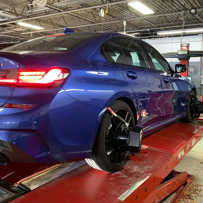 Blue sports sedan on a lift in an auto repair shop, rear-left view.