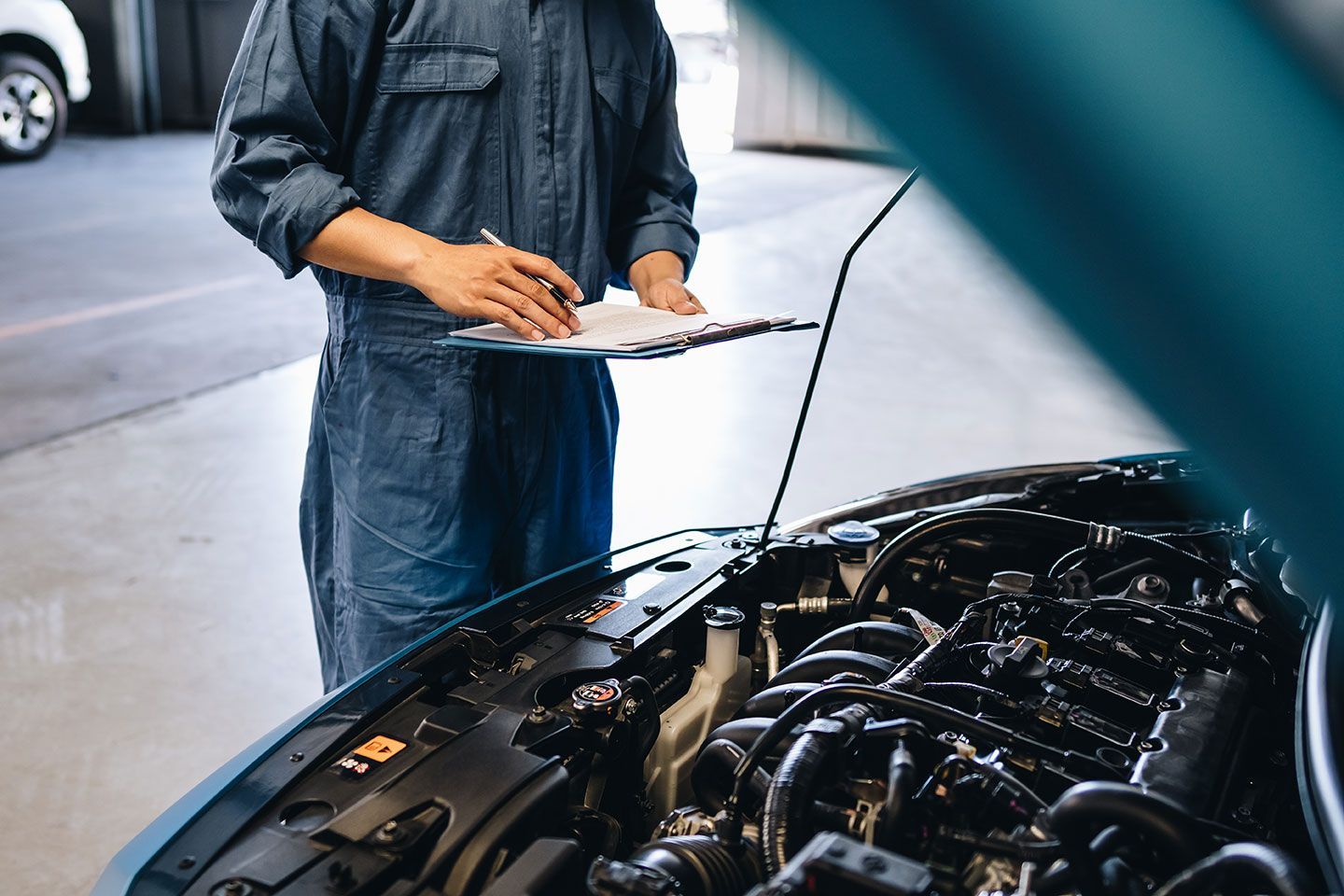 Mechanic with clipboard inspecting a car engine in a garage