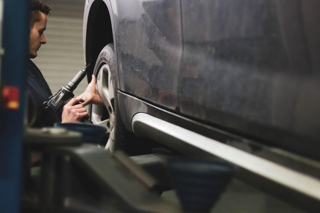Mechanic inflating a car tire beside a dark vehicle in a garage