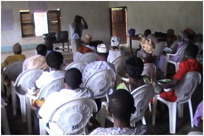 Audience seated in a small meeting room facing a speaker at the front