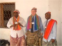 Three people standing indoors, wearing colorful traditional clothing and scarves.