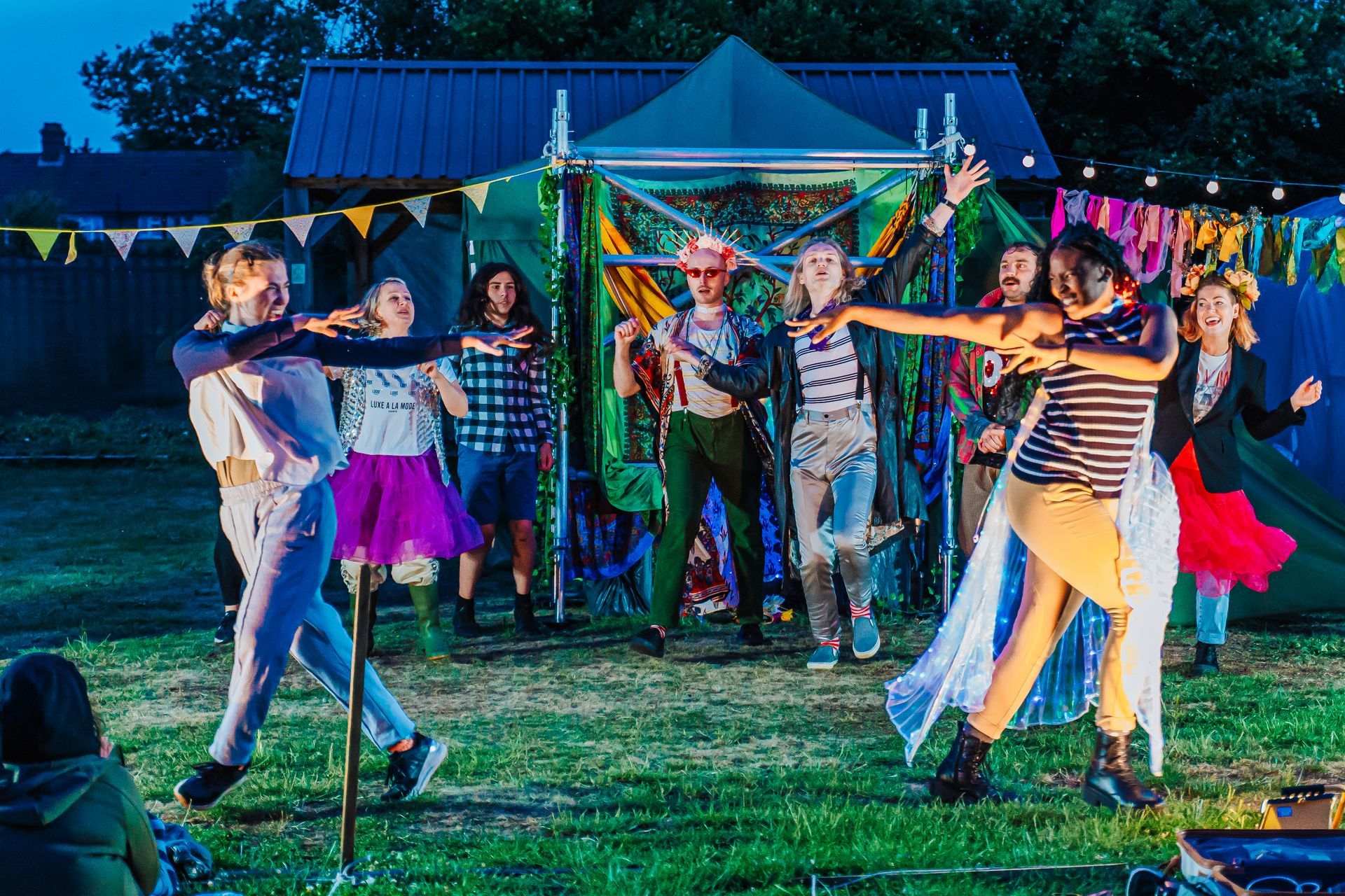 People dancing outdoors at night under colorful lights near a small tent booth