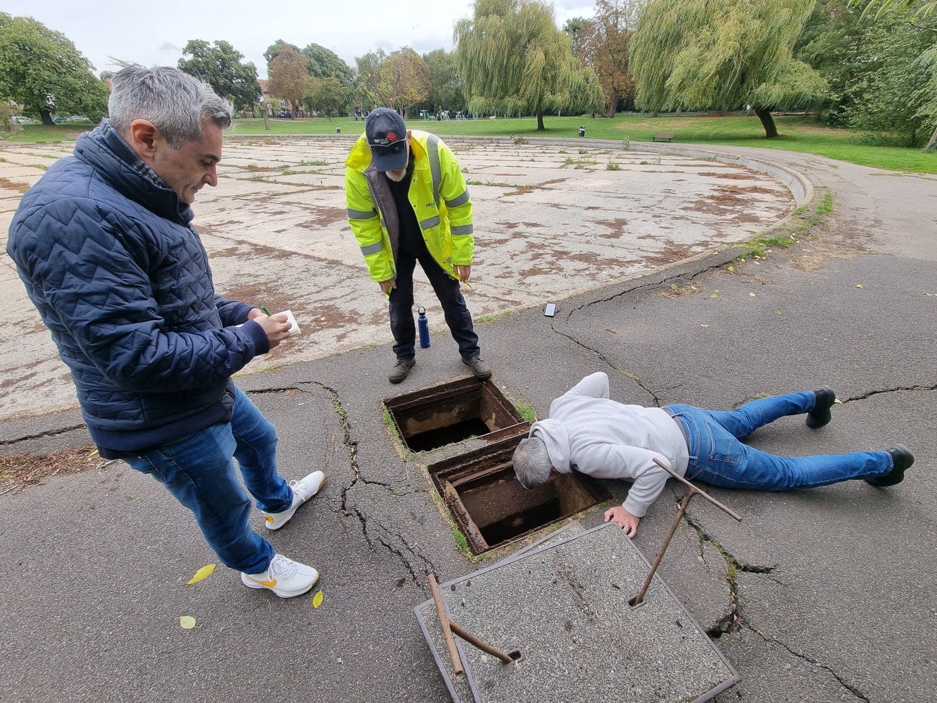 A man is laying on the ground next to a manhole cover.