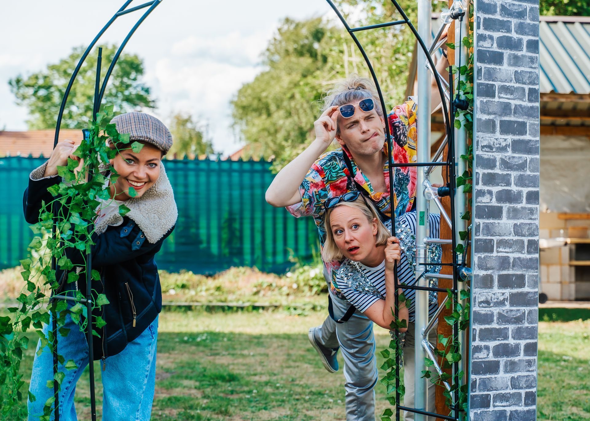 Three people peeking playfully through a garden arch in a grassy yard