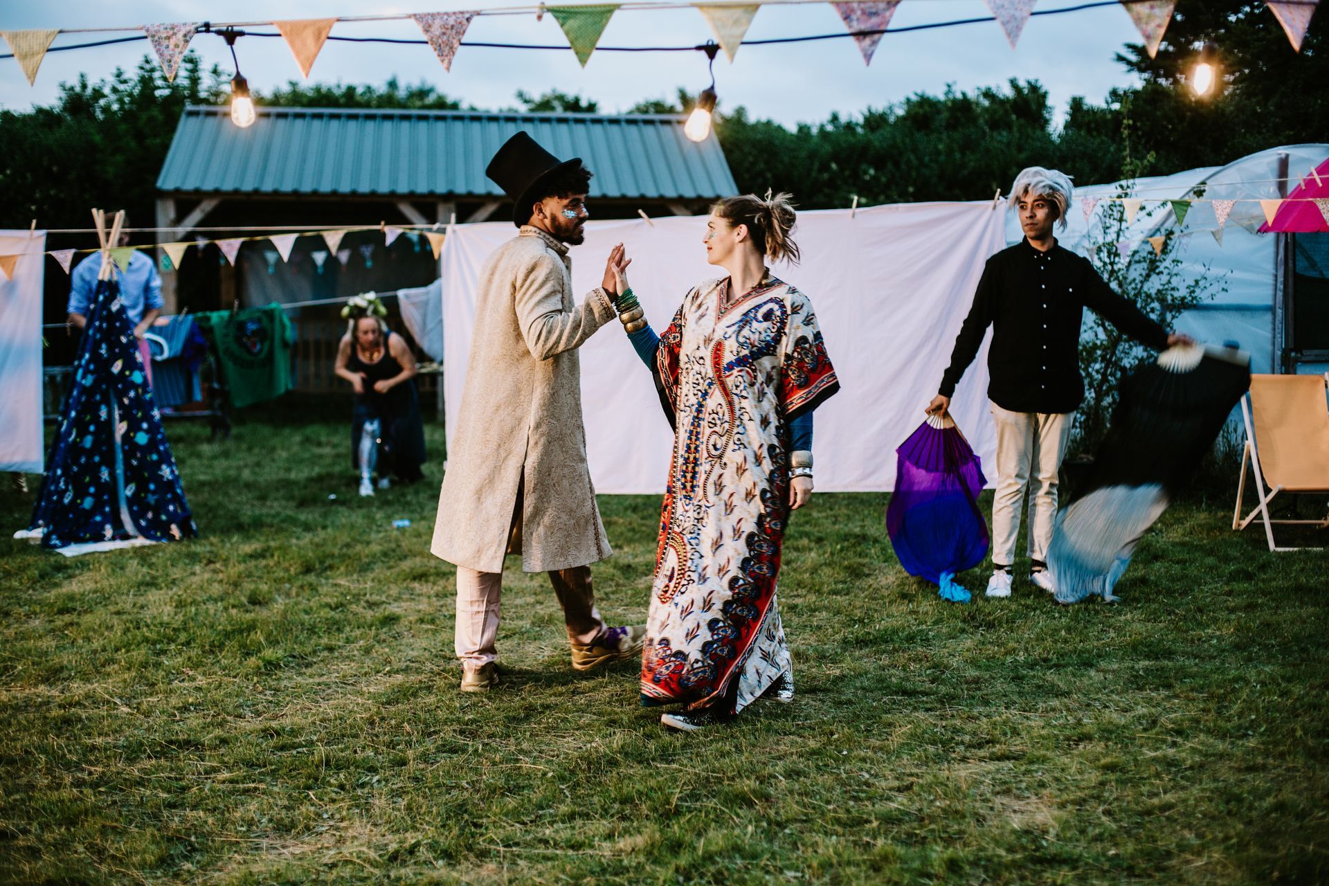 People dancing outdoors at a colorful festival with bunting and tents in the background