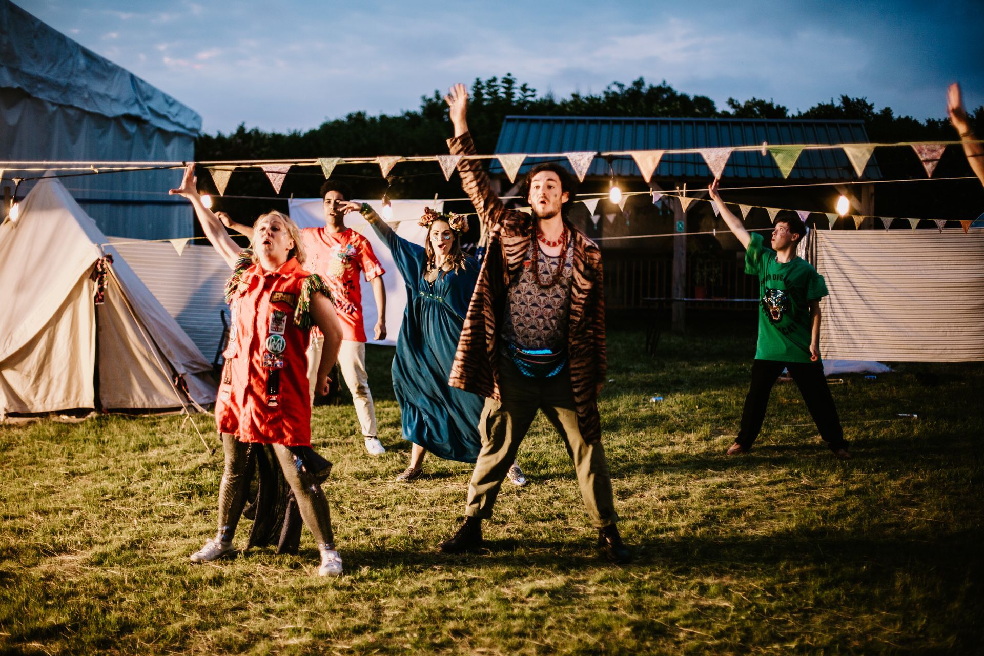 People dancing outdoors at a nighttime festival beside tents and string bunting
