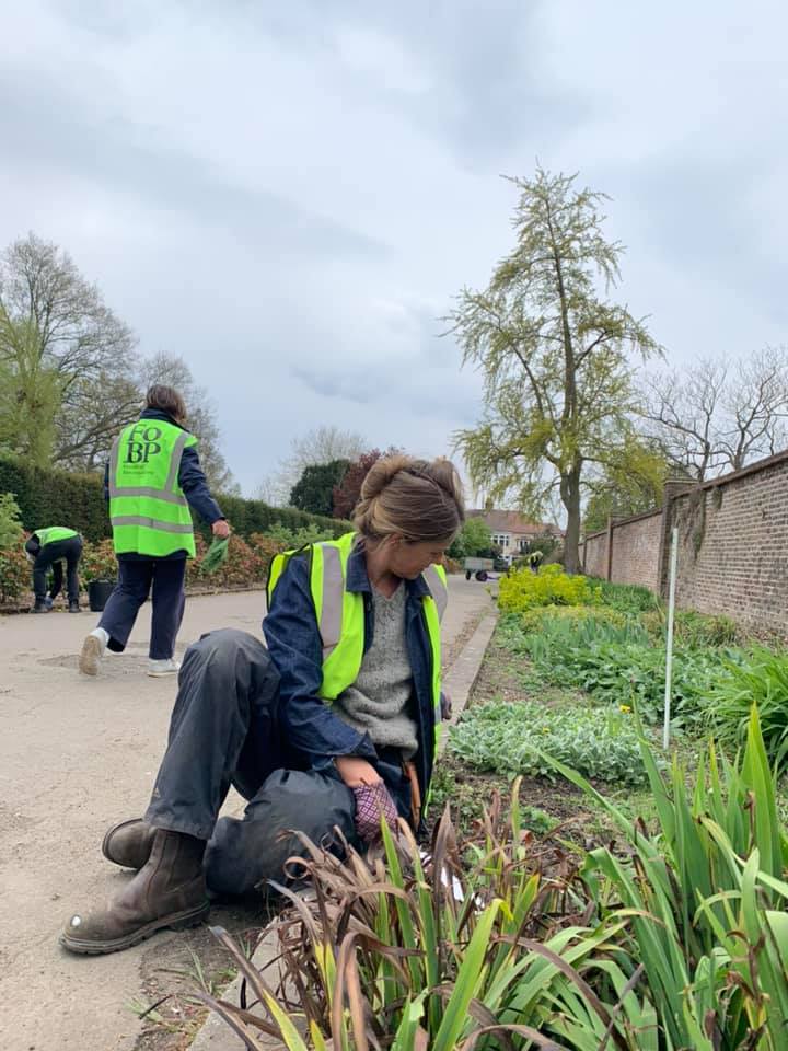 A woman in a yellow vest is sitting on the ground in a garden.