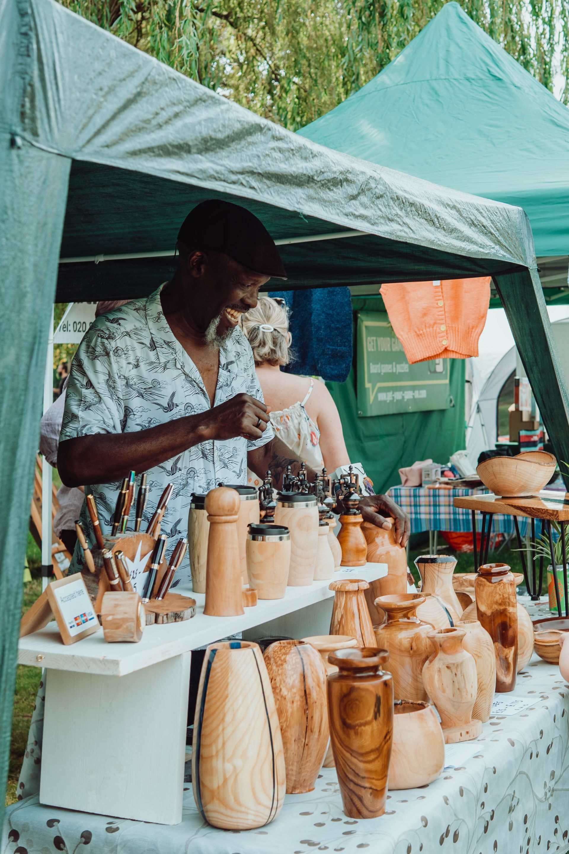 A man is standing in front of a tent selling wooden vases.