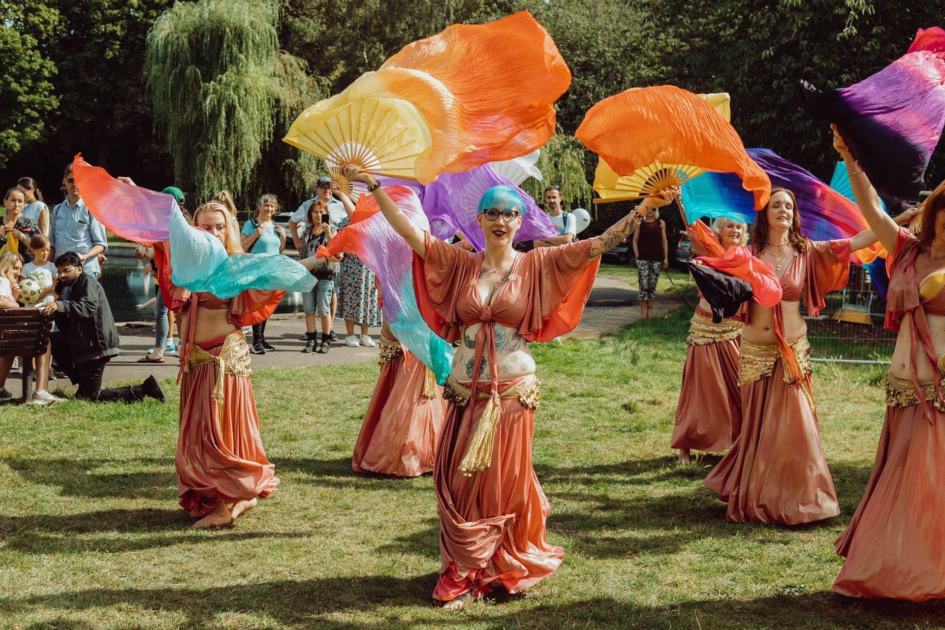 A group of belly dancers are dancing in a park with colorful fans.