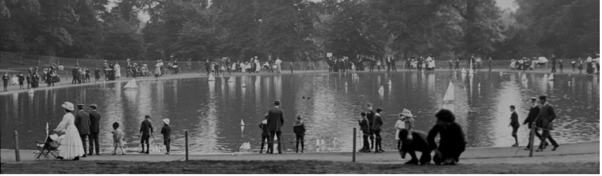 A black and white photo of a group of people standing around a lake.