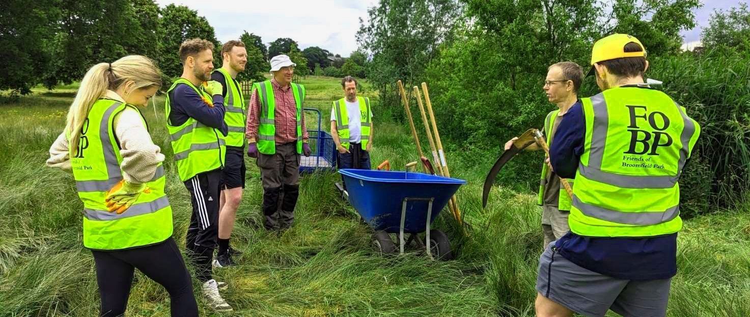 People in high-vis vests tending to a green space, with tools and a blue wheelbarrow visible.