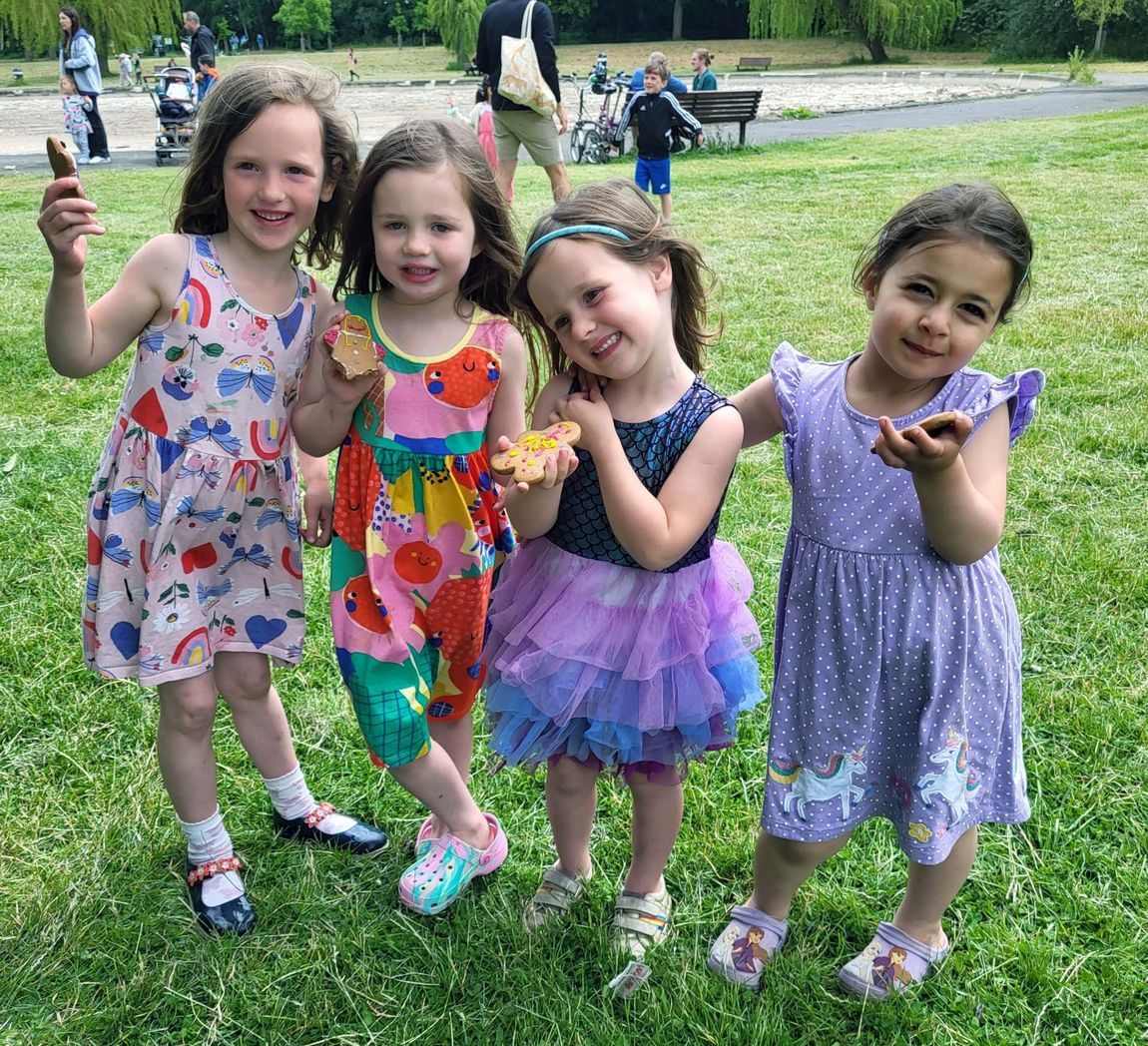 Four children in colorful dresses pose and smile on a grassy lawn, holding up flowers.