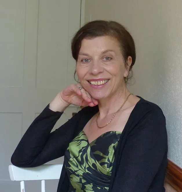 A woman wearing a black cardigan and a green dress smiles for the camera