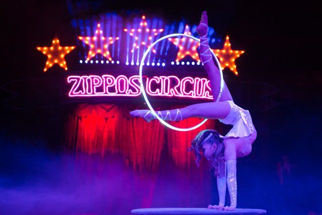 A woman is doing a handstand in front of a sign that says zippo 's circus.