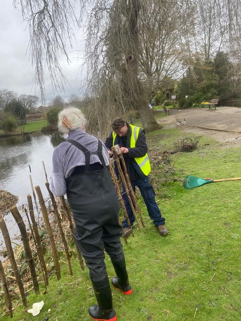 A man and a woman are working on a wooden fence in a park.