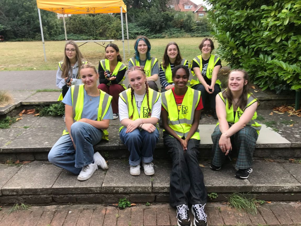 Group of people in neon safety vests posing on outdoor steps under an orange canopy.
