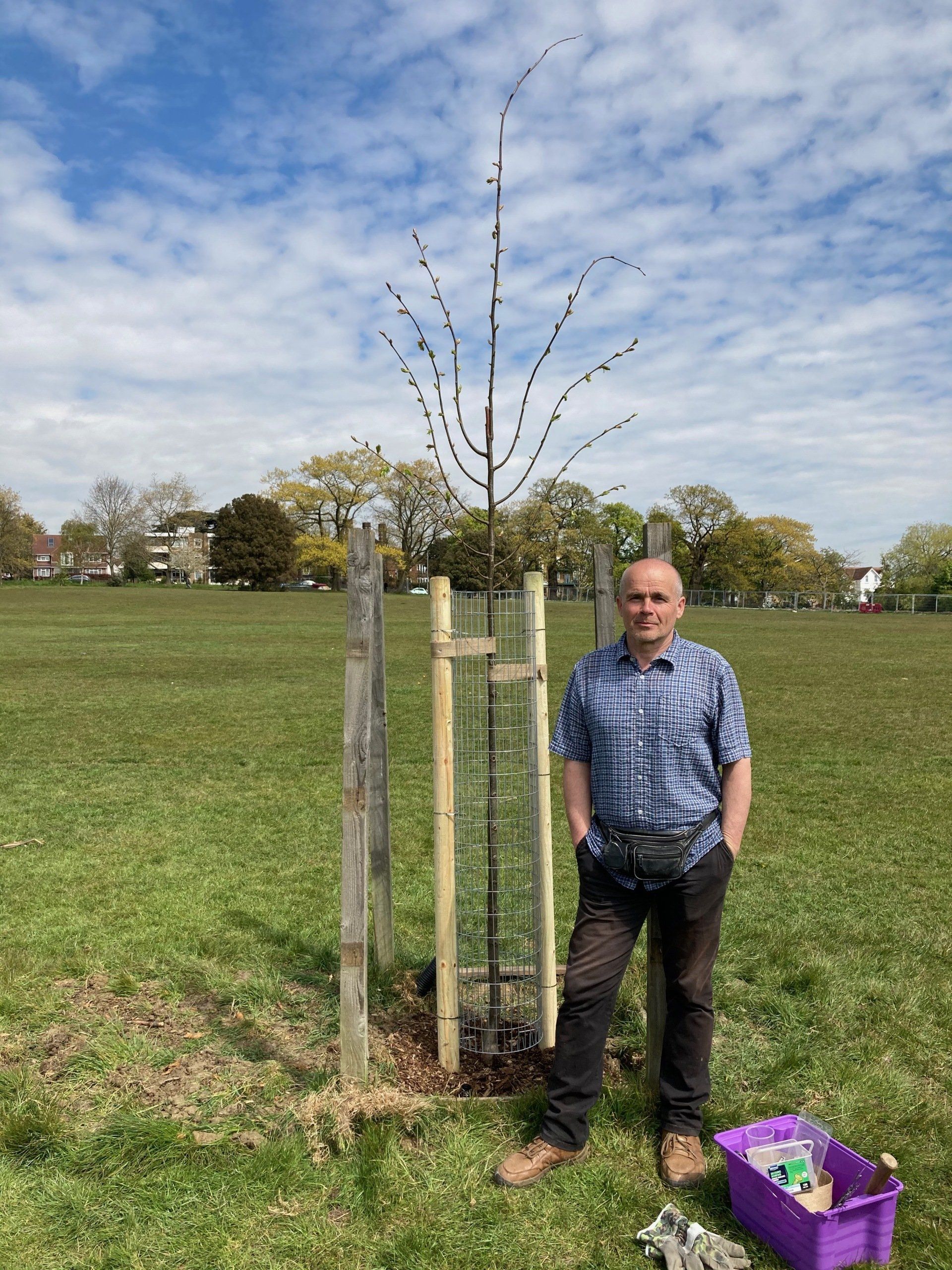 A man is standing next to a tree in a field.