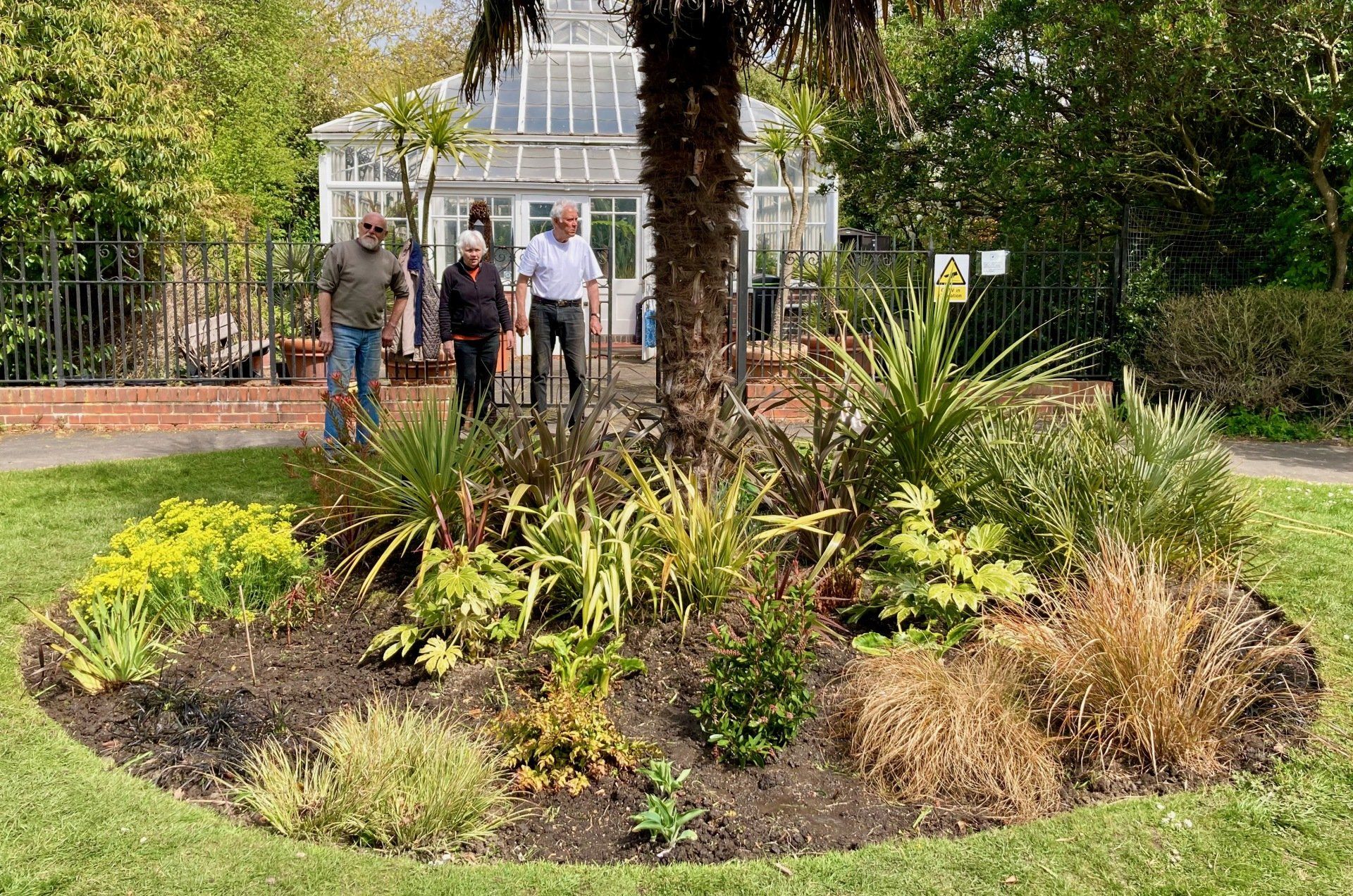 A group of people are standing around a garden in a park.