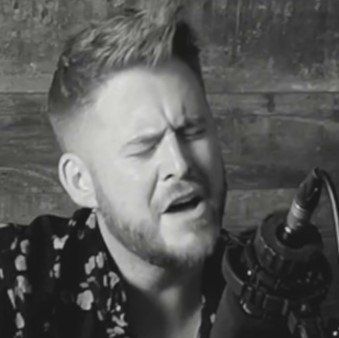 A man with a beard is singing into a microphone in a black and white photo.