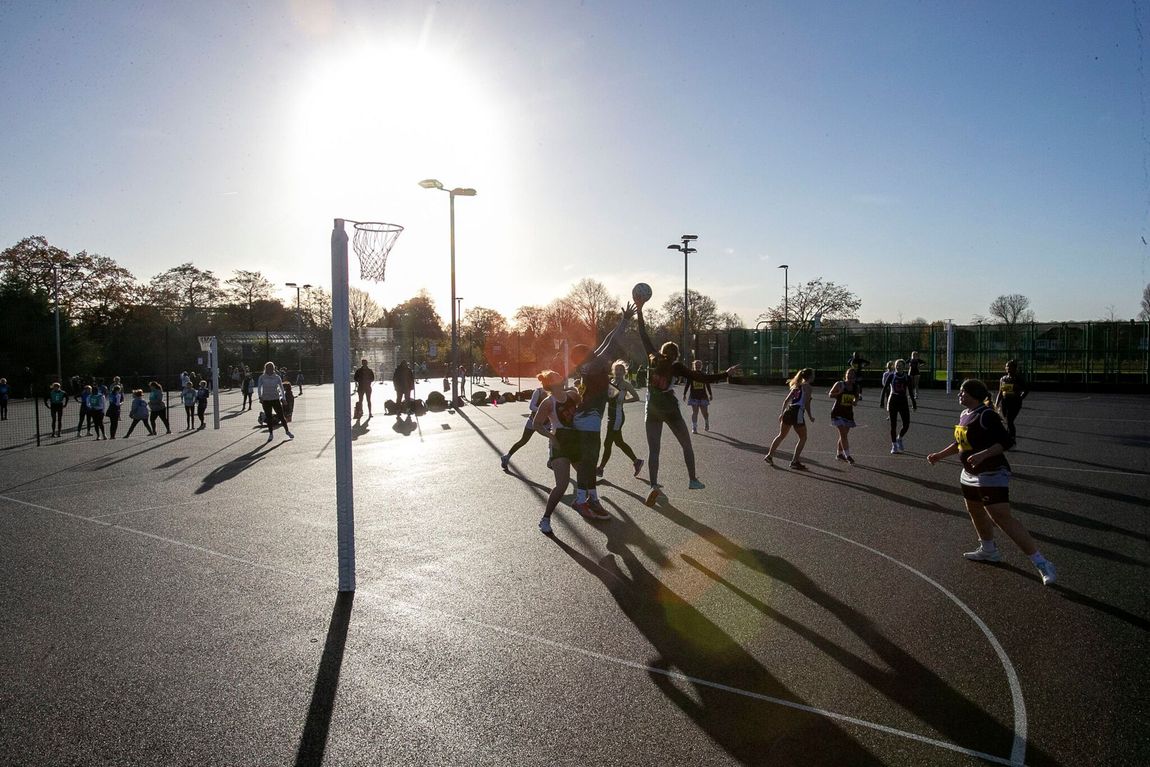 People playing lacrosse on an outdoor court at sunset, with long shadows and bright sunlight.