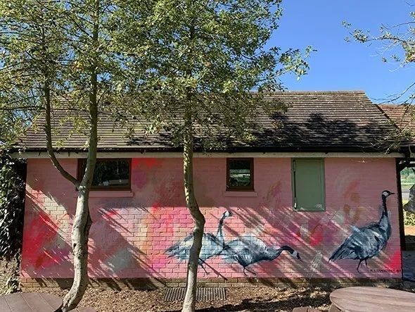 A pink building with a painting of birds on the side of it.