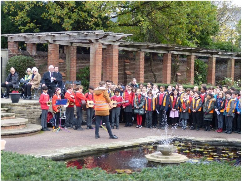 A group of children are standing in front of a fountain.