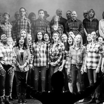 A large group of people are singing together on a stage in a black and white photo.
